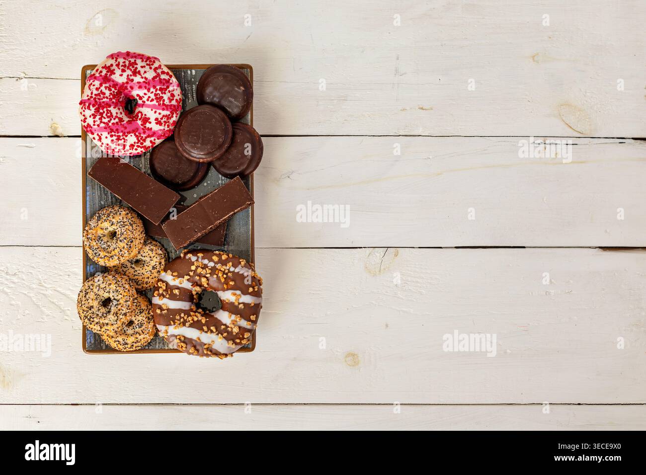Verschiedene Donuts Und Schokoladenbonbons Auf Dem Tablett. Blick von oben auf verschiedene Donuts, Schokoladenkekse und Desserttafeln auf einem Tablett mit Kopierraum Stockfoto