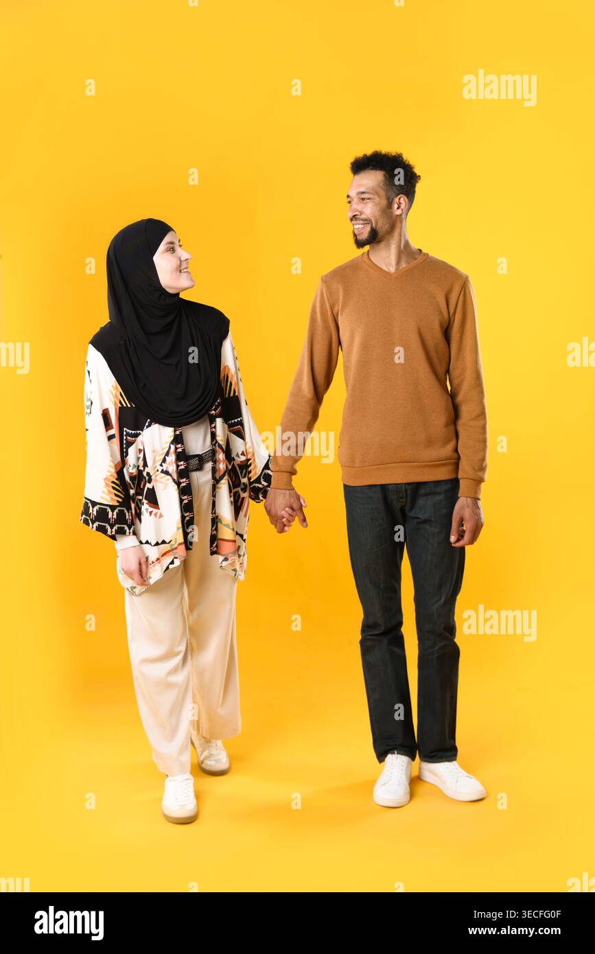 Glückliches muslimisches Paar, das Hände auf gelbem Hintergrund hält Stockfoto