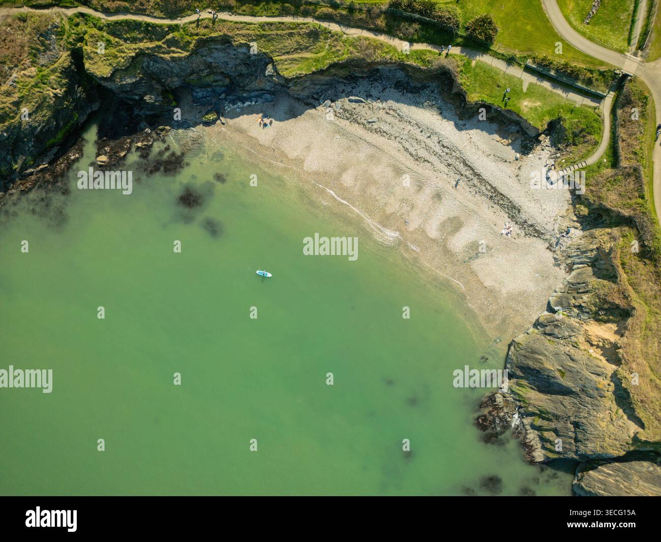 Blick aus der Vogelperspektive auf einen abgelegenen Sandstrand, eingebettet zwischen felsigen Klippen mit einem Paddelboarder im türkisfarbenen Wasser und Menschen, die sich am Ufer in WIC entspannen Stockfoto