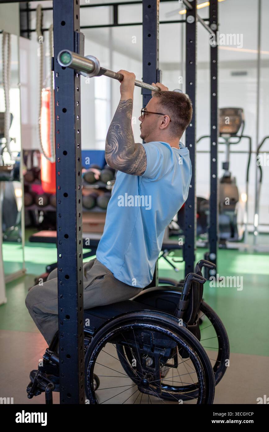 Mann im Rollstuhl beim vertikalen Pull-Up-Training mit adaptiven Fitnessgeräten im Sportzentrum. Stockfoto