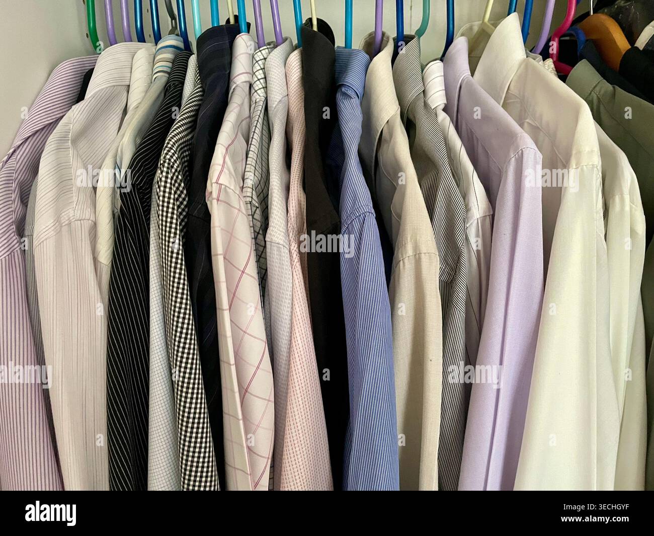 Eine Sammlung von professionellen Hemden in verschiedenen Farben auf farbigen Kleiderbügeln - Smartphone-aufgenommenes Stockfoto