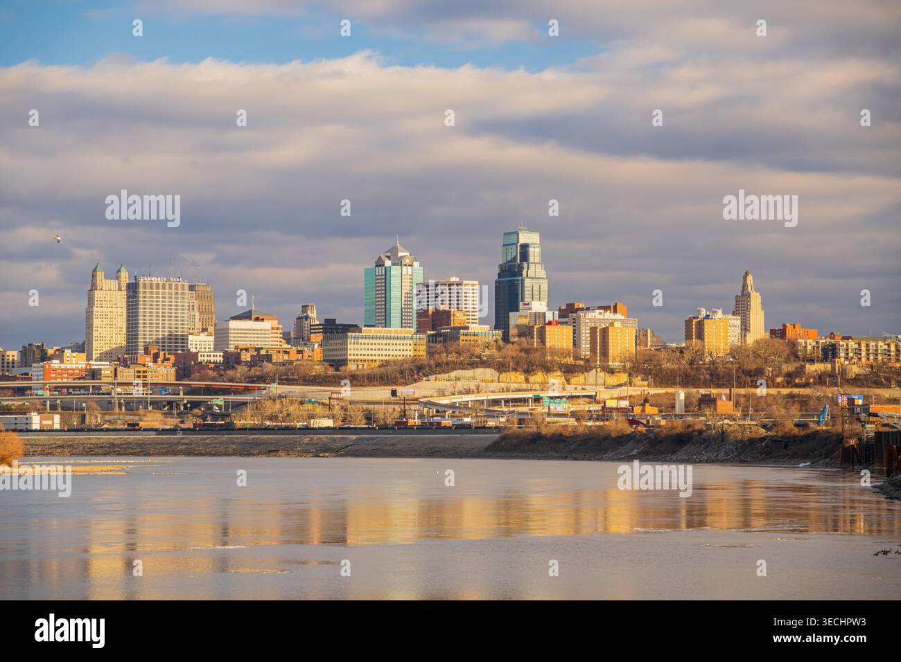 Moderne Wolkenkratzer und urbane Architektur ragen über einem Flussufer unter einer riesigen Weite aus weichen, farbenfrohen Wolken hervor. Stockfoto