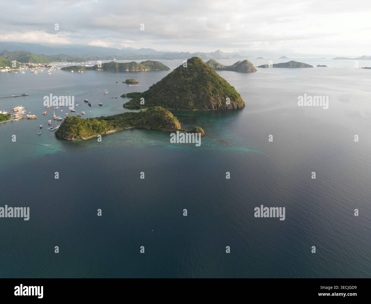 Aus der Vogelperspektive auf üppig grüne tropische Inseln und Boote, die im türkisfarbenen Wasser der Bucht nahe Flores unter einem weichen, bewölkten Himmel in Labuan ankern Stockfoto