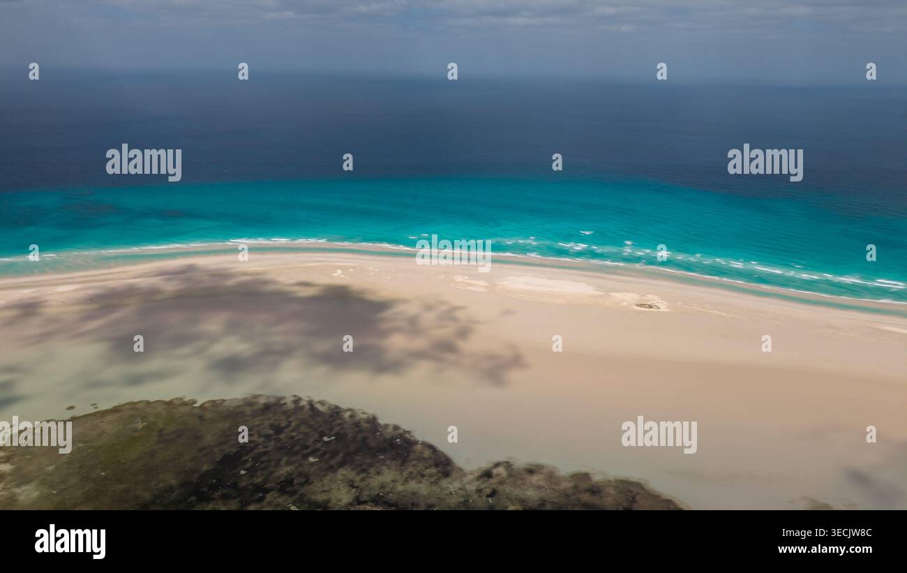 Aus der Vogelperspektive auf einen abgeschiedenen tropischen Strand mit weißem Sand, türkisfarbenem Meer, sanften Wellen und weichen Wolkenschatten unter einem bewölkten Himmel. Detwah Lagune, Stockfoto