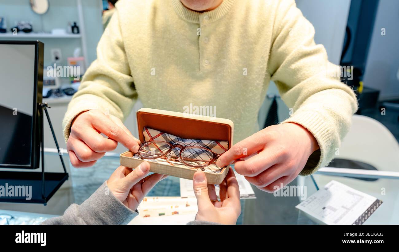 Ein Optiker unterstützt einen zufriedenen Kunden in einem optischen Zentrum und präsentiert eine Brille in einem stilvollen Etui. Die Interaktion unterstreicht die Zufriedenheit der Kunden Stockfoto
