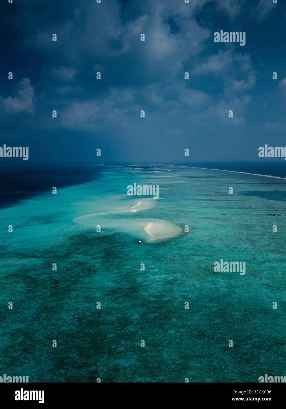 Dramatischer Blick aus der Luft auf eine Lagune der Malediven mit türkisfarbenem Wasser, Korallenriff und heller Sandbank unter dunklen Sturmwolken mit tropischen Einflüssen Stockfoto