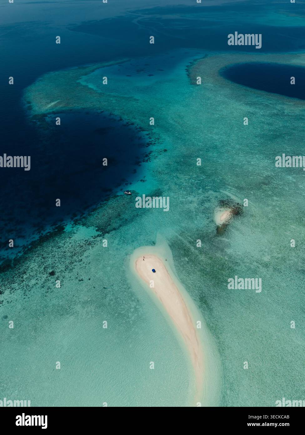 Drohne aus der Vogelperspektive einer Sandbank auf der Insel Malediven, die sich durch eine türkisfarbene Lagune und ein tiefblaues Meer mit Korallenriffstrukturen, einem kleinen Boot und einer ruhigen tropi kurvt Stockfoto