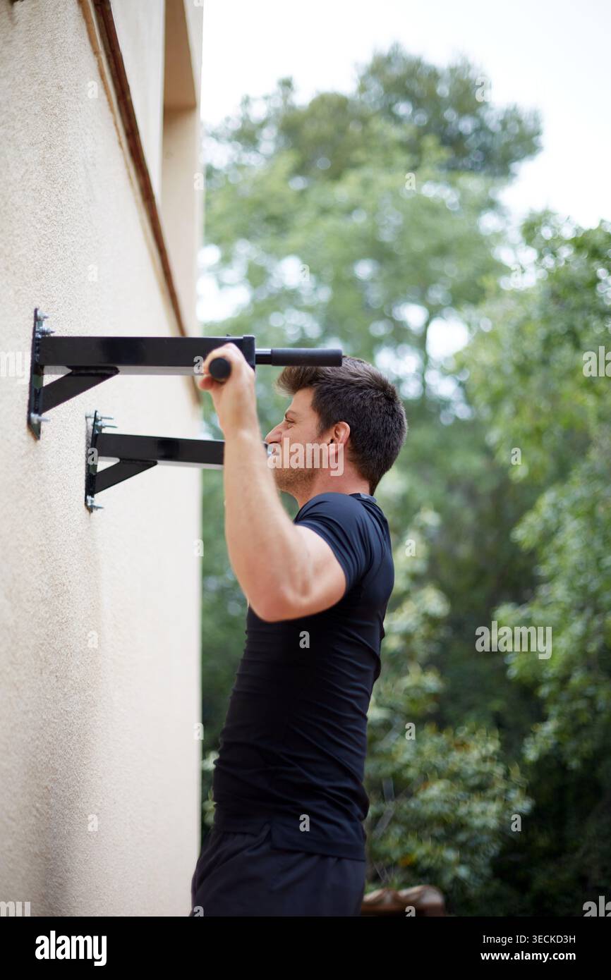 Sportliche Mann-Übungen auf einer Outdoor-Pull-up-Bar an einer Wand montiert, ein Workout für Kraft und Ausdauer, fokussiert auf Fitness, Gesundheit und s Stockfoto