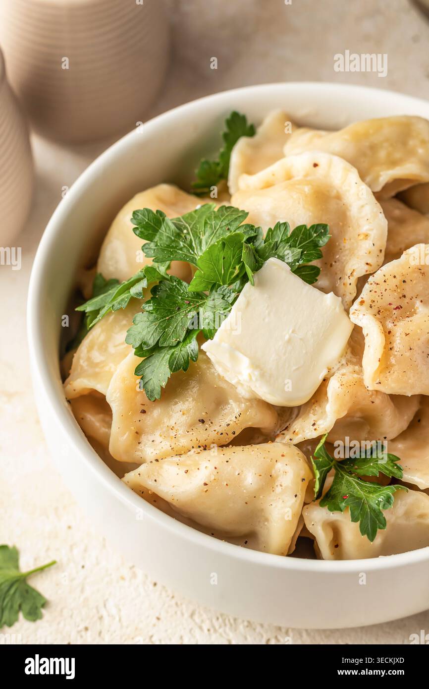 Hausgemachte Fleischknödel oder Pelmeni serviert mit Butter und frischer Petersilie in einer weißen Schüssel. Vertikal Stockfoto