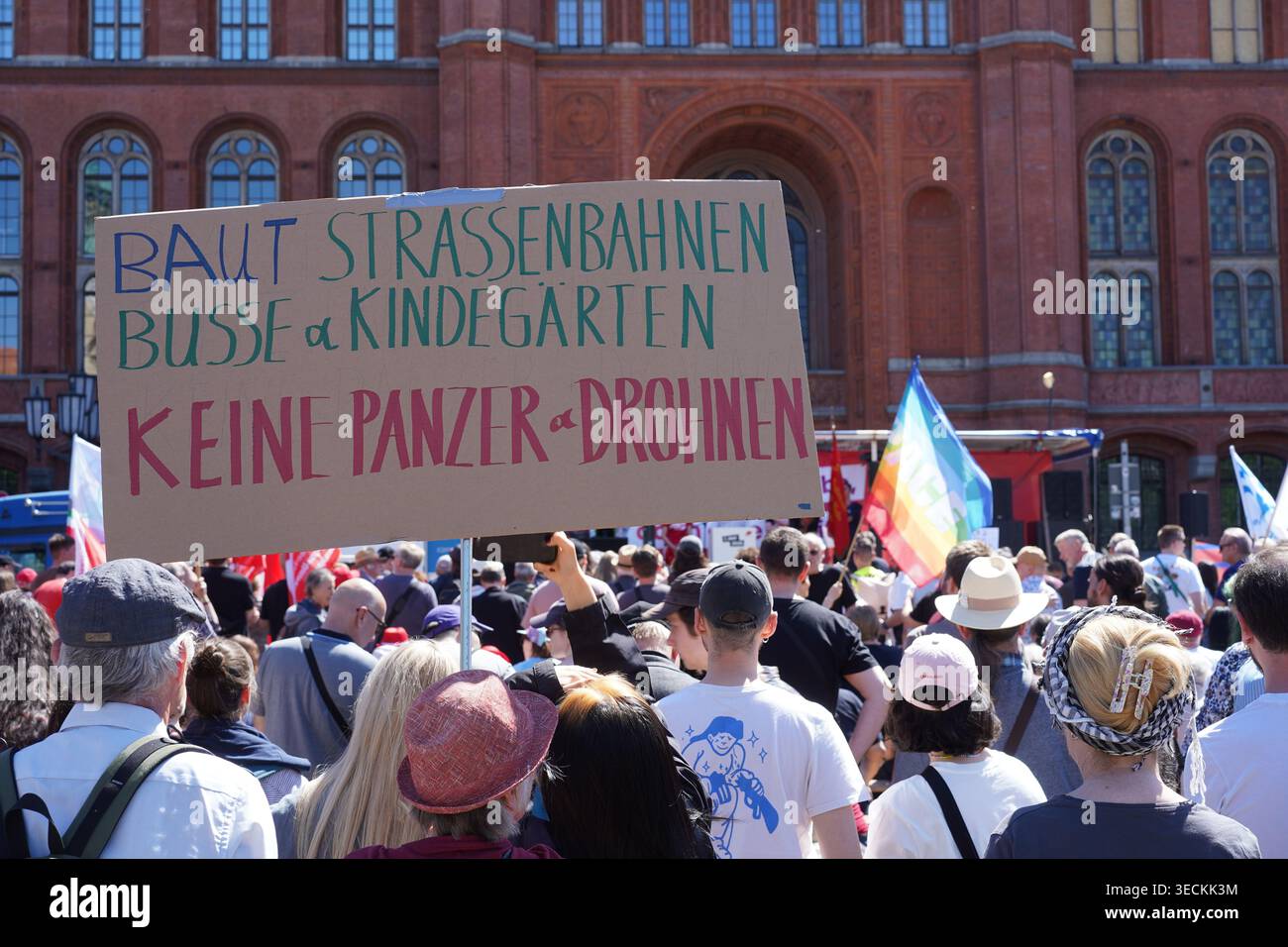 Berlin – 1. Mai 2026: Ein Demonstrant hält ein handgefertigtes Pappschild, das Sozialausgaben für militärische Investitionen im Roten Rathaus fordert. Stockfoto