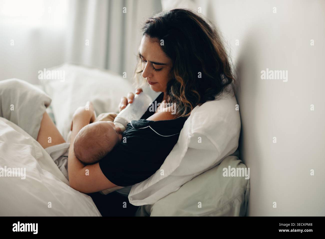 Eine fürsorgliche Mutter füttert ihr Baby mit der Flasche, während sie bequem sitzt und in einer ruhigen häuslichen Atmosphäre die pflegende Elternschaft zeigt. Stockfoto