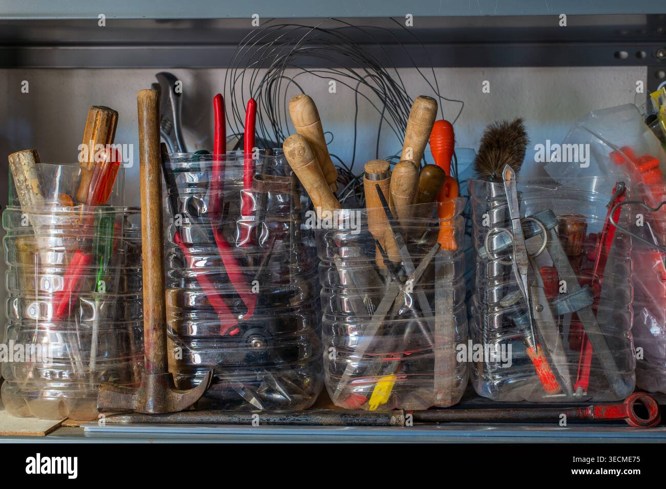 Verschiedene Handwerkzeuge, einschließlich Hämmer, Zangen, Schraubendreher und Metallgeräte, die in wiederverwendeten Kunststoffbehältern auf einem Werkstattregal gelagert werden Stockfoto