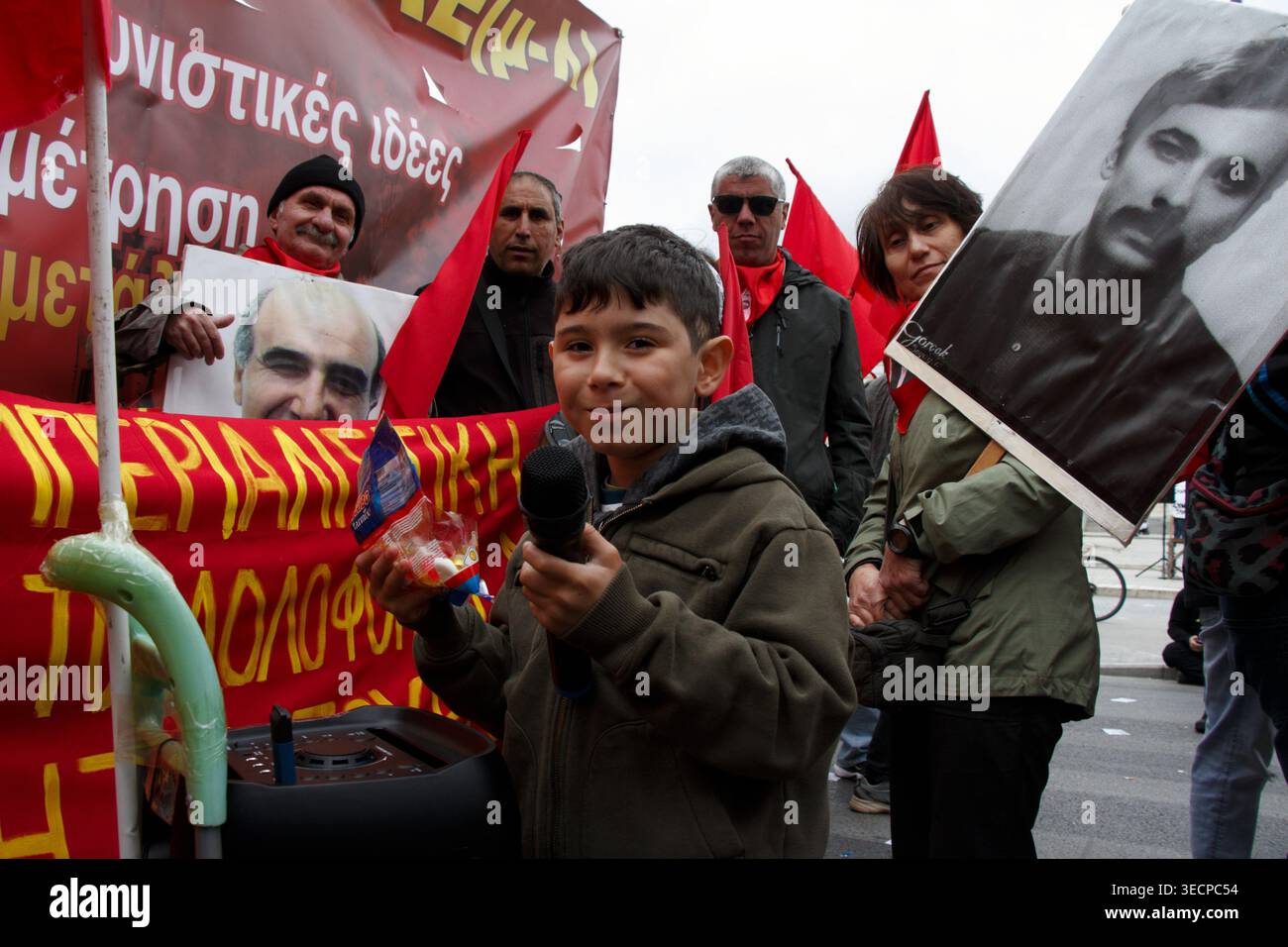 Ein Kind hält während eines Maiprotests in Athen ein Mikrofon, während Erwachsene dahinter Fahnen und Plakate tragen. Athen, Griechenland | Mai 2026 Stockfoto