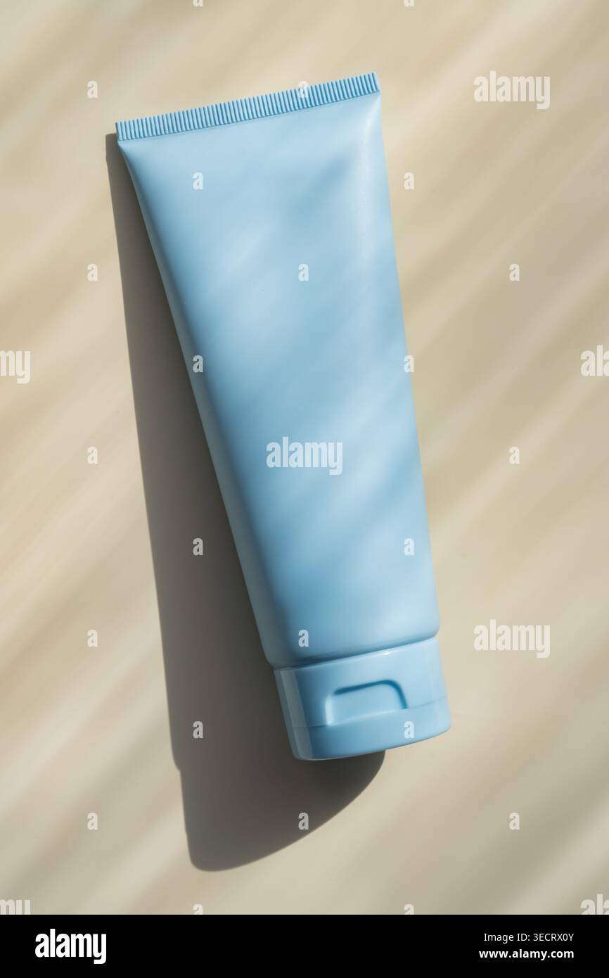 Minimales Studiofoto einer blauen Kosmetikcremeflasche auf beigefarbenem Hintergrund mit natürlichem Licht und weichem Schatten, ideal für Hautpflege-Branding, Mocku Stockfoto
