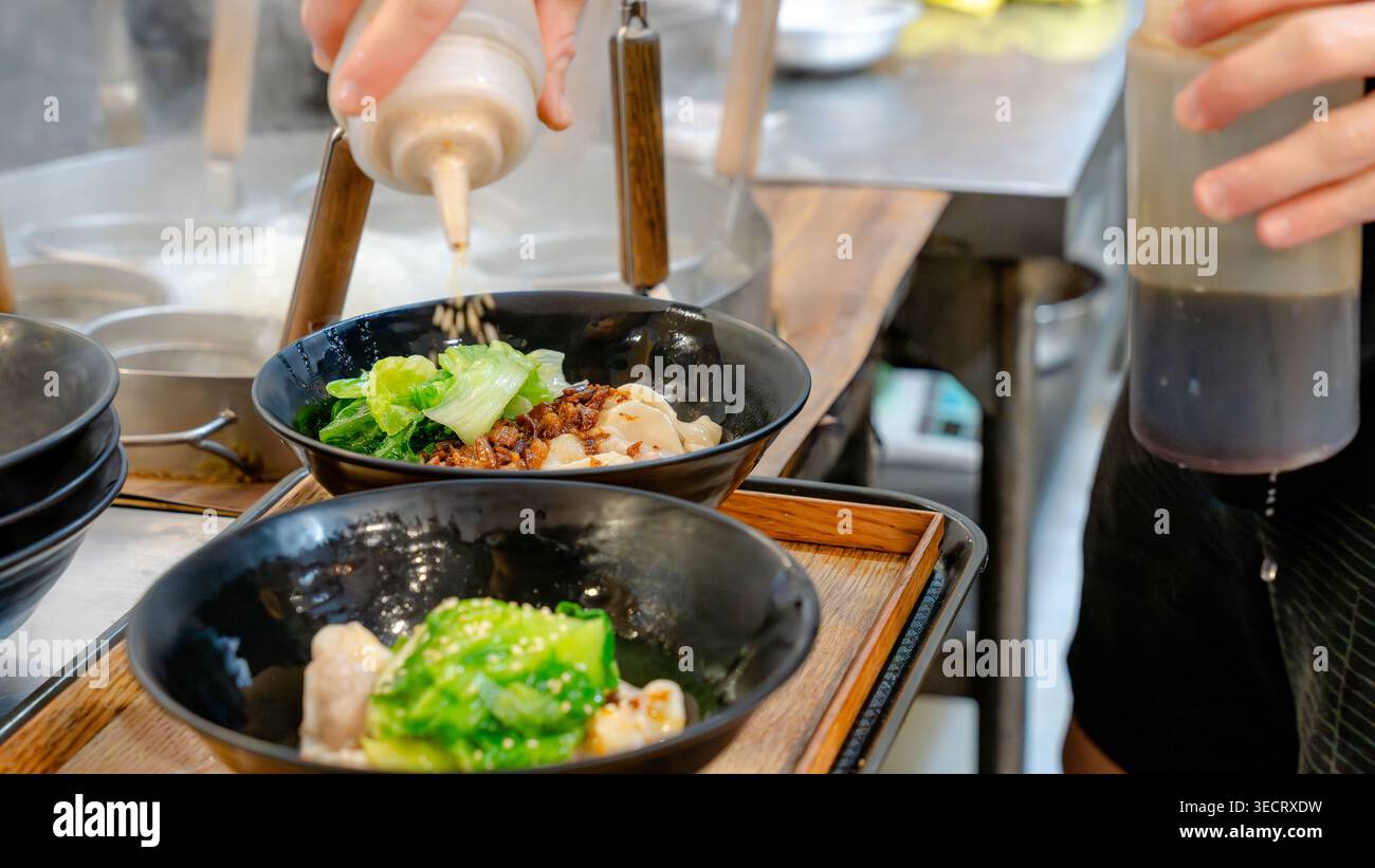 Ein Küchenchef verleiht einem taiwanesischen Gericht in einer belebten Restaurantküche gekonnt den letzten Schliff und fängt die Essenz traditioneller Aromen und Kuhgerichte ein Stockfoto