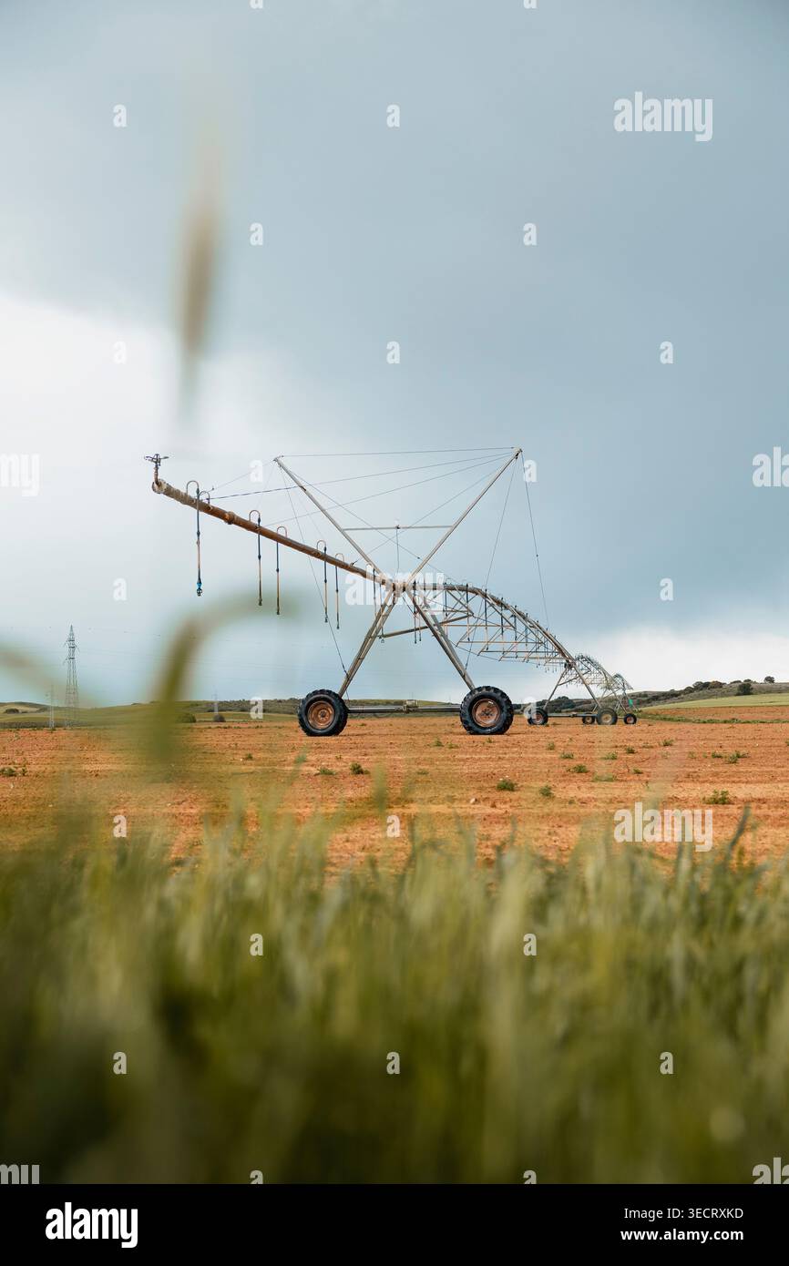 Das zentrale Pivot-Bewässerungssystem erstreckt sich über ein trockenes Ackerfeld unter bewölktem Himmel und zeigt moderne Landwirtschaft Wasserwirtschaft, Pflanzenproduktion, Stockfoto