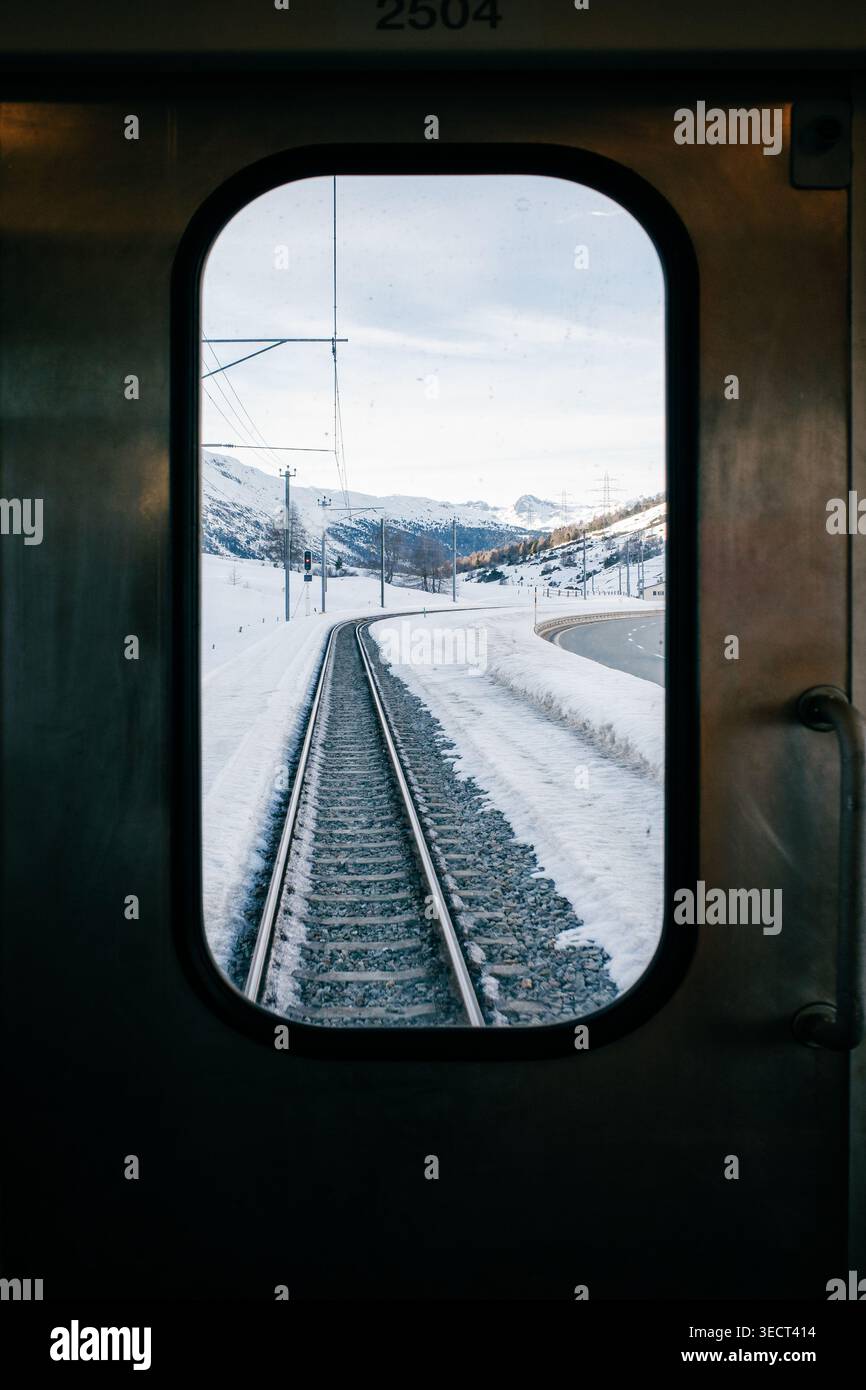 Blick von einem Zugfenster auf eine wunderschöne schneebedeckte europäische Landschaft. Die Bahngleise kurven sanft durch den unberührten Schnee, mit weit entfernten Moun Stockfoto