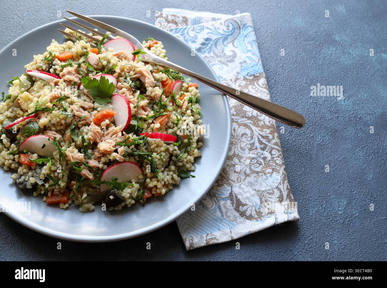 Gesunder mediterraner Couscous-Salat mit Thunfisch, frischem Rettich und Petersilie auf blauem Hintergrund. Couscous Tabbouleh. Mediterranes Ernährungskonzept. Stockfoto