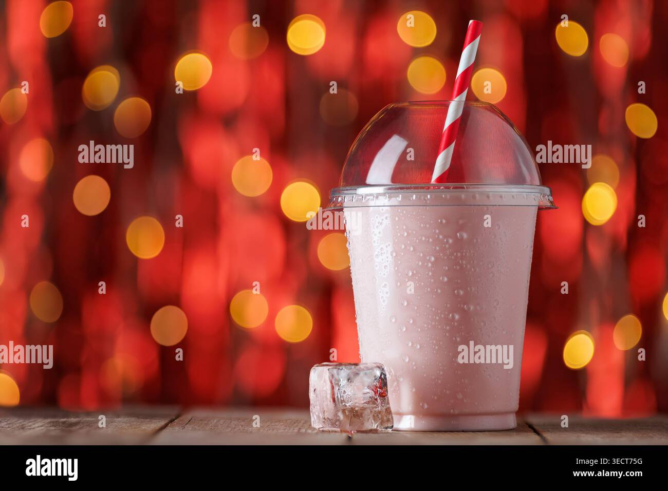 Erdbeeren-Milchshake in Einweg-Plastikbecher mit Kondenswasser und rot-weiß gestreiftem Stroh auf Holzoberfläche Stockfoto