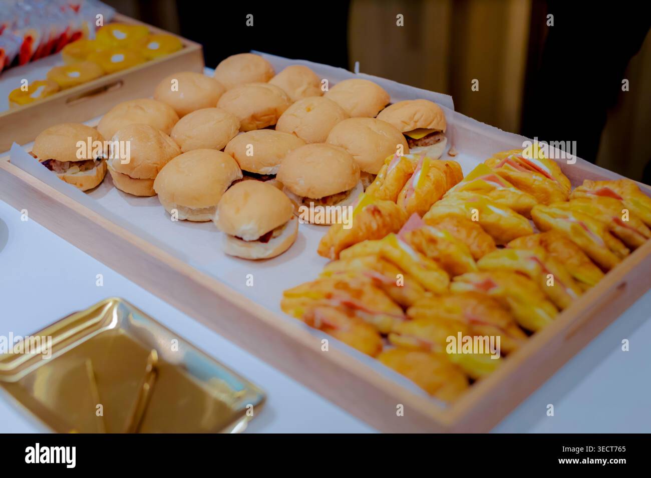 Mini-Slider und Croissant-Sandwiches, ordentlich auf einem hölzernen Catering-Tray für ein Hotel-Buffet angeordnet. Stockfoto