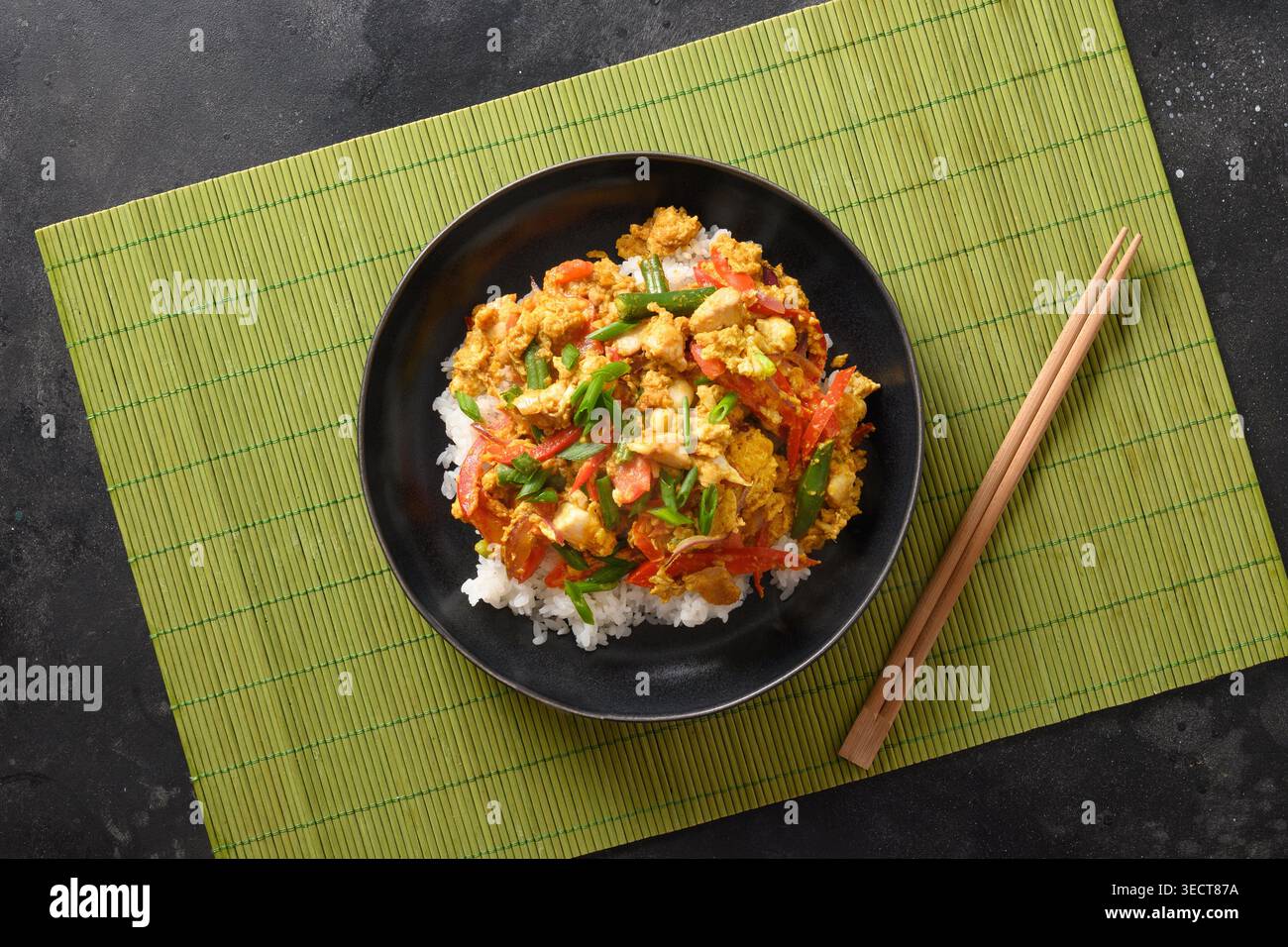 Thailändisches Frühstück Gai Pad Pongali mit Hühnchen, Eiern, scharfer, gelber thai-Currypaste, Tomaten, Reis in schwarzer Schüssel aus Wok. Nahaufnahme. Panasiatische Küche. Thailändisches Essen Gebraten. Stockfoto