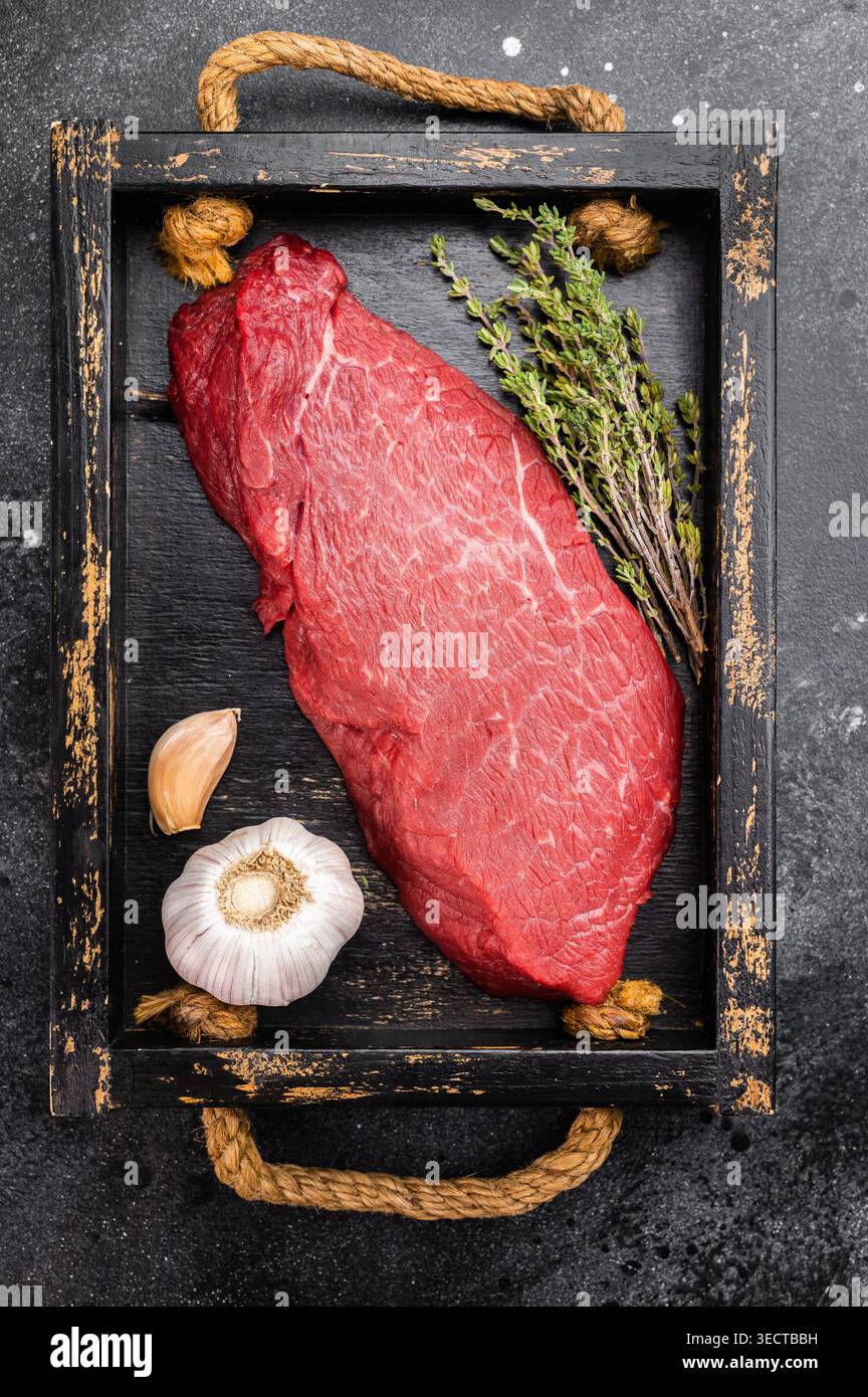 Frisches rohes Rindfleisch innen rund oben mit Thymiankraut und Knoblauch auf Holztablett. Fettarmes Fleisch auf dunklem Hintergrund, Draufsicht. Stockfoto