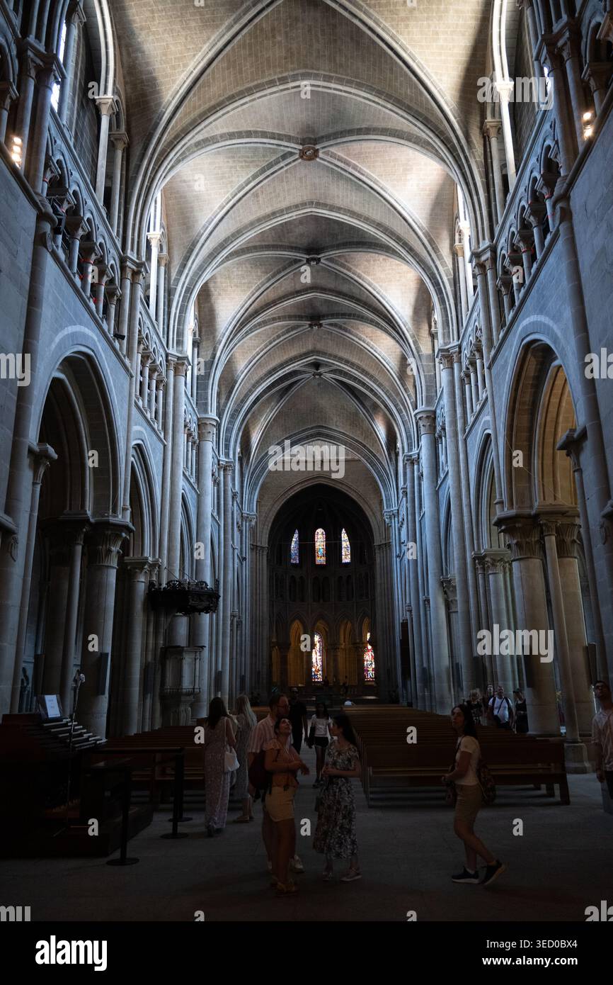 Innenraum eines gotischen Kirchenschiffs in Lausanne, Schweiz, mit Rippengewölben, Steinsäulen, Buntglas, und Besucher in sanftem Licht. Stockfoto