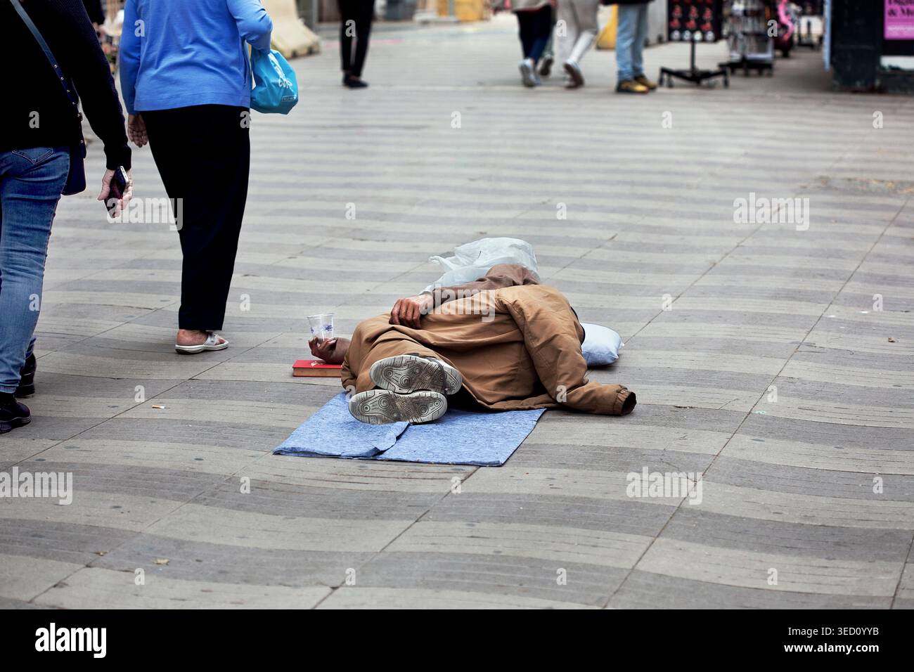 Touristen gehen an einem bettelnden Mann in Las Ramblas, Barcelona, Spanien vorbei. Stockfoto