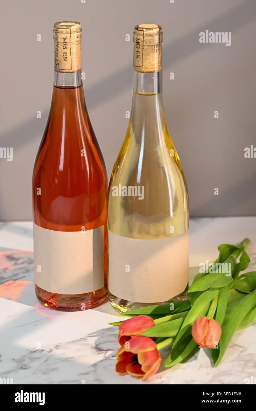Zwei Flaschen Wein stehen neben frischen Tulpen auf Marmor. Stockfoto