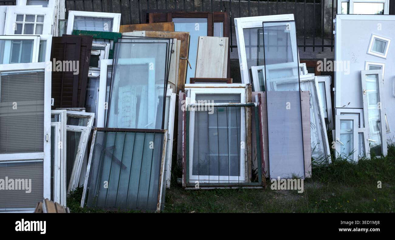 Ein großer Haufen verschiedener alter Fensterrahmen und Glasscheiben, die draußen gegen einen Zaun gelehnt sind. Stockfoto
