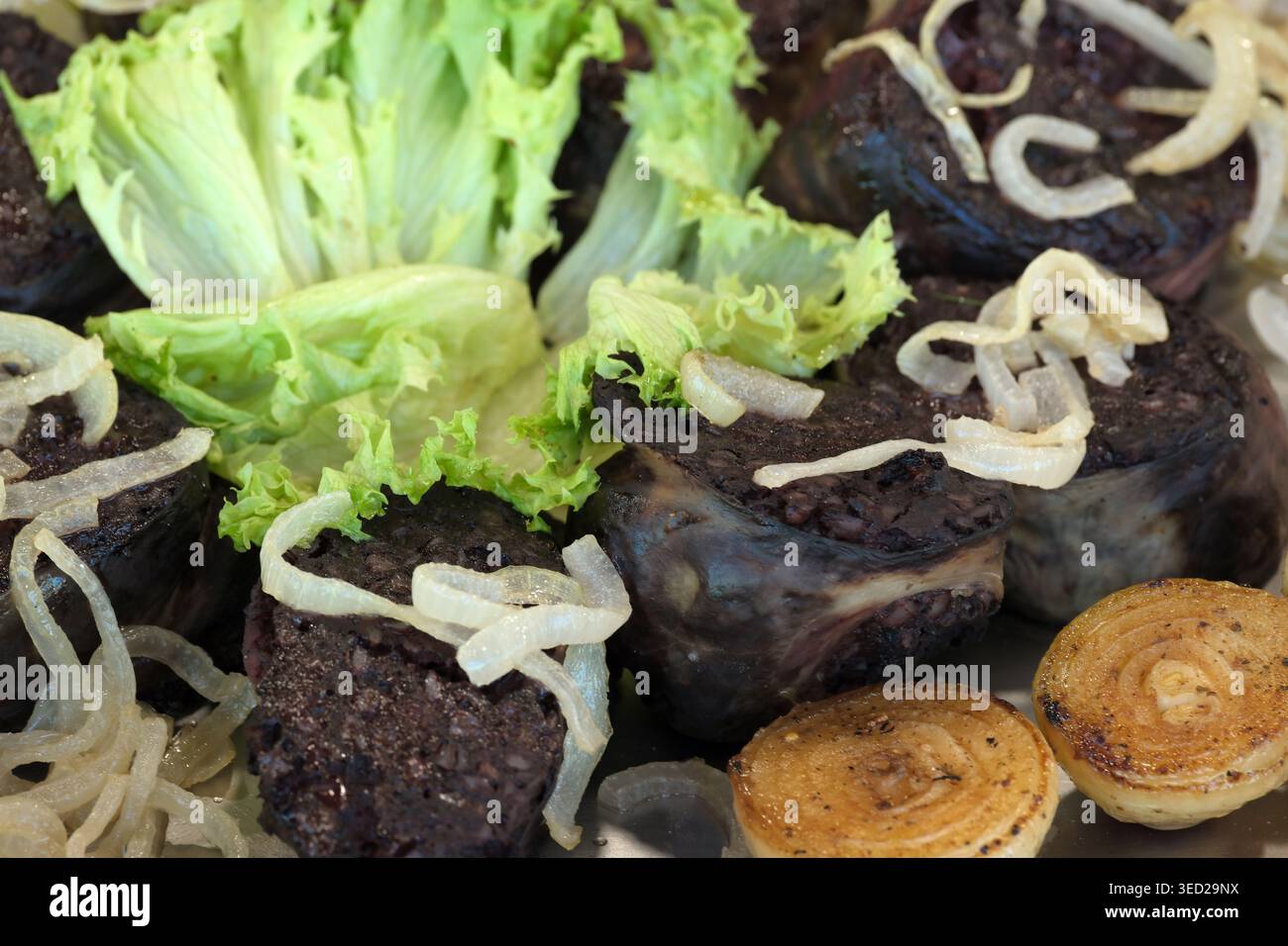 Schwarzer Pudding, wunderschön arrangiert mit frischem Salat und karamelisierten Zwiebeln an der Seite. Stockfoto