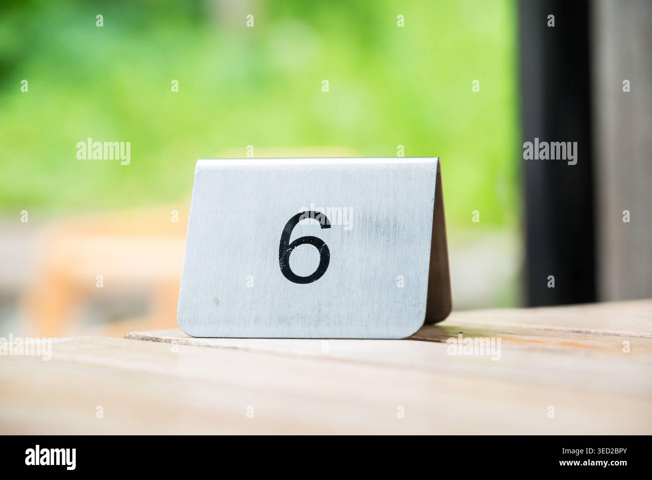 Der Tisch aus gebürstetem Metall Nr. 6 liegt auf einer hellen Holzoberfläche mit einem unscharfen grünen Hintergrund. Stockfoto
