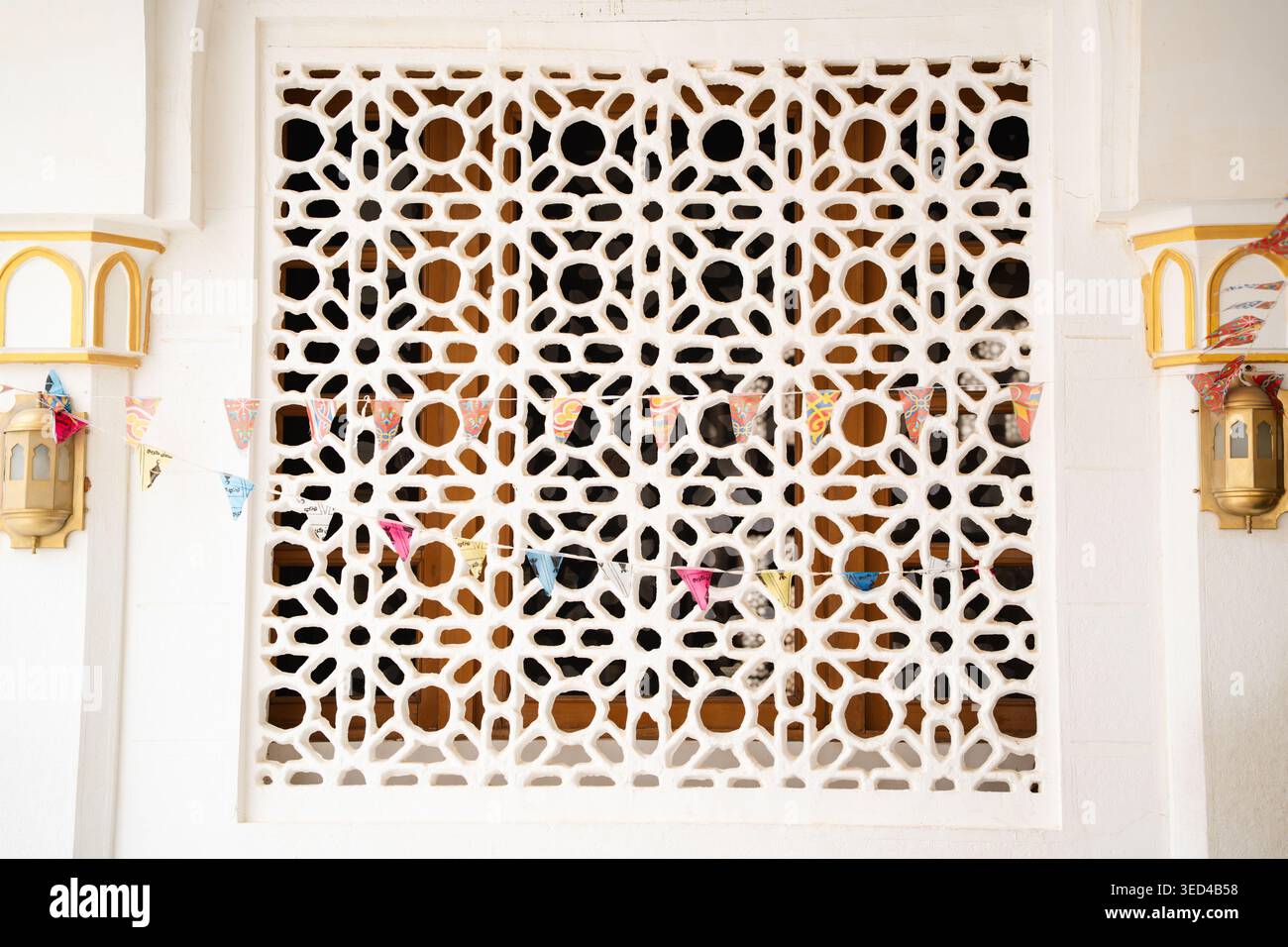 Dekorative Moschee-Mashrabiya-Fensterscheibe mit geometrischem Arabesken-Muster und bunten hängenden Fahnen an der weißen Wandfassade. Islamische Architektur, tra Stockfoto