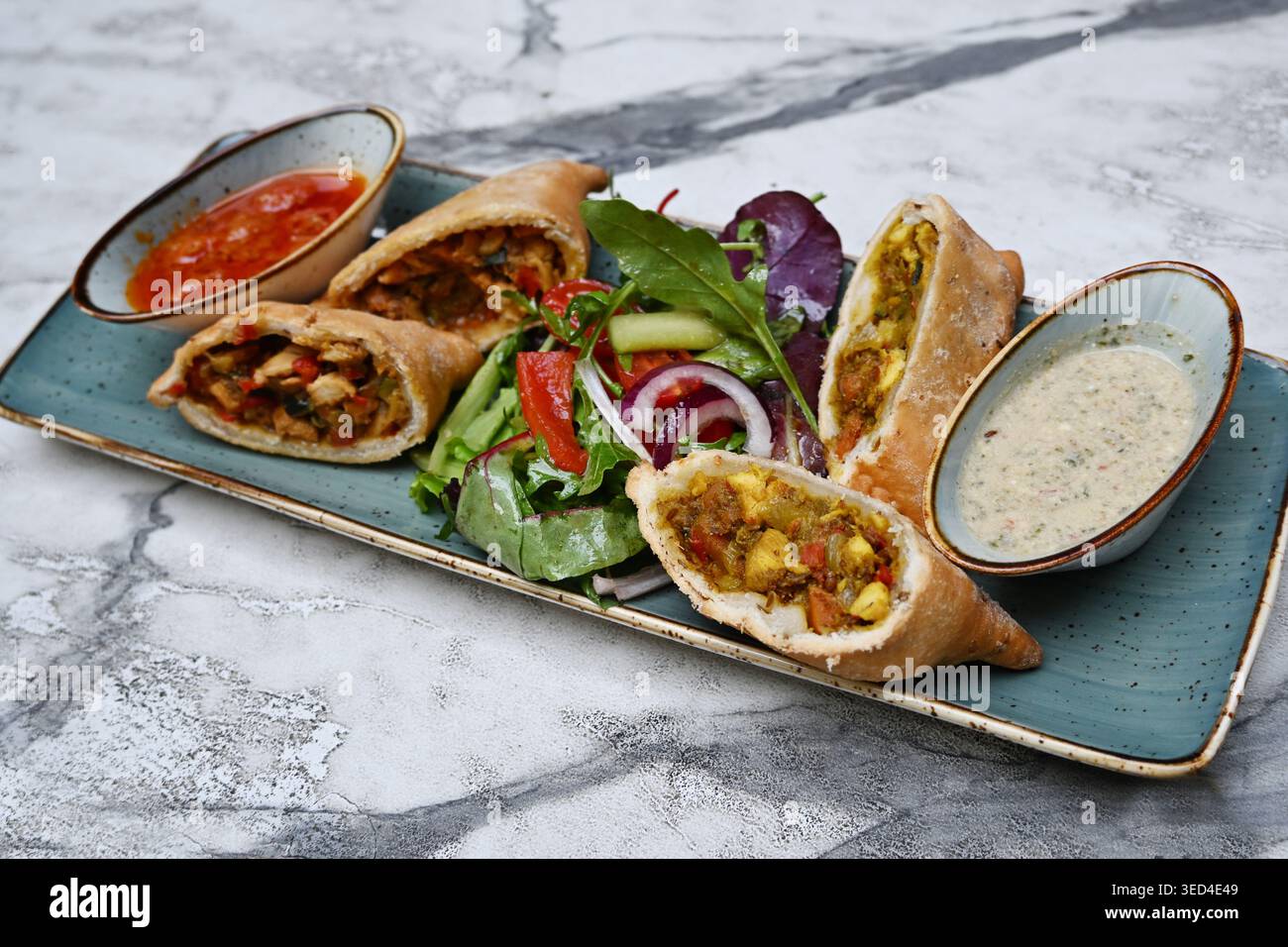 Samosa, gebratenes indisches oder persisches Dreiecksgebäck mit einer Füllung aus Gemüse, Huhn und Gewürzen, serviert mit zwei Dips und Salat, traditionelles Street-Fo Stockfoto