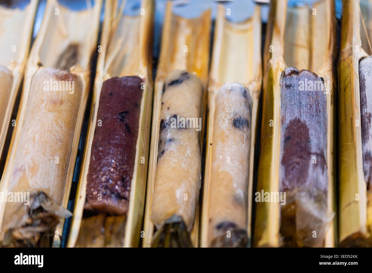 Nahaufnahme von klebrigen Reisrollen, die in Bambusröhren gegrillt werden und traditionelle Street Food Textur rauchiger Geschmack natürliche Kochmethode zeigen Stockfoto