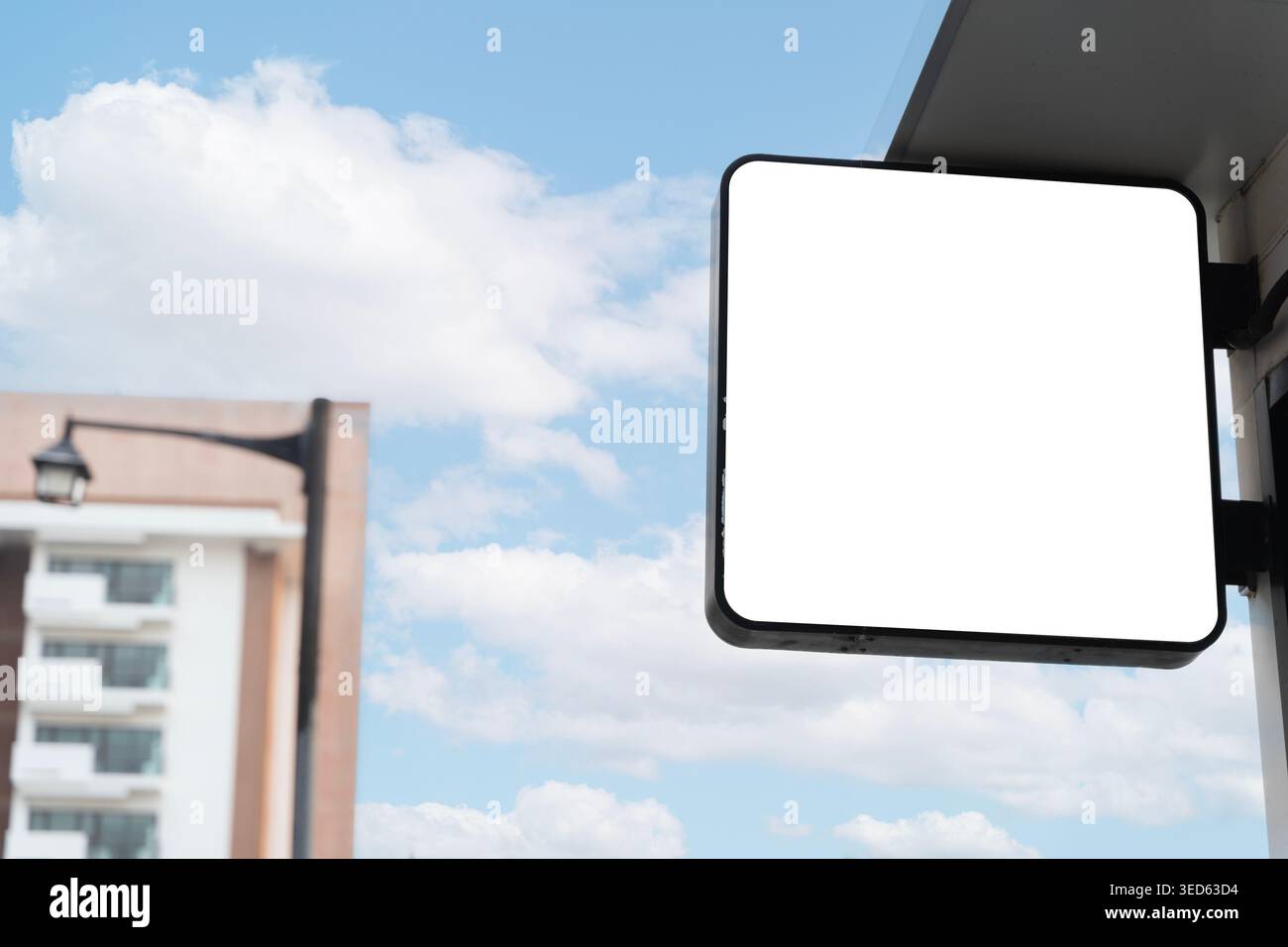 Leeres quadratisches Ladenfront-Schild an einer Gebäudeaußenwand mit blauem Himmel und weichem urbanem Hintergrund, ideal für Einzelhandelsmarken, Logodisplays und Werbung Stockfoto
