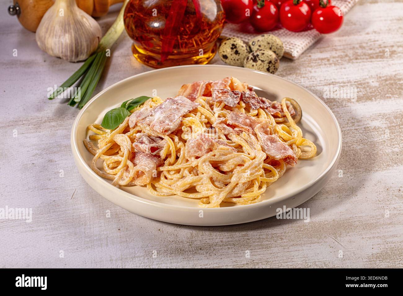 Appetitliche Spaghetti Carbonara serviert auf weißem Teller. Eine reichhaltige cremige Sauce umhüllt Nudeln, garniert mit knusprigem Speck und frischem Basilikum. Rustikaler Hintergrund Stockfoto