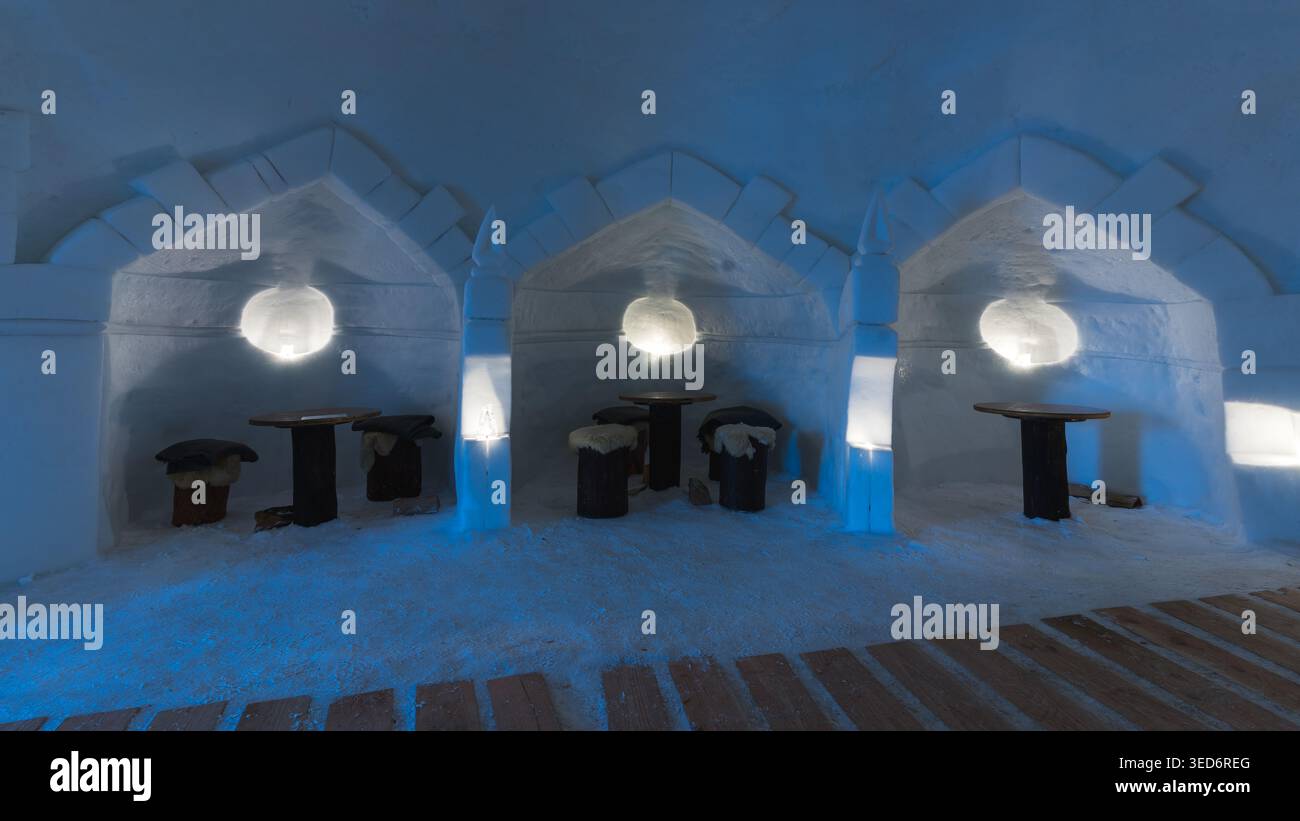 Eine beleuchtete Eishöhle in Zermatt, Schweiz, mit drei gebogenen Nischen und Tischen, die in ein kühles, ätherisches blaues Licht getaucht sind. Der Architec Stockfoto