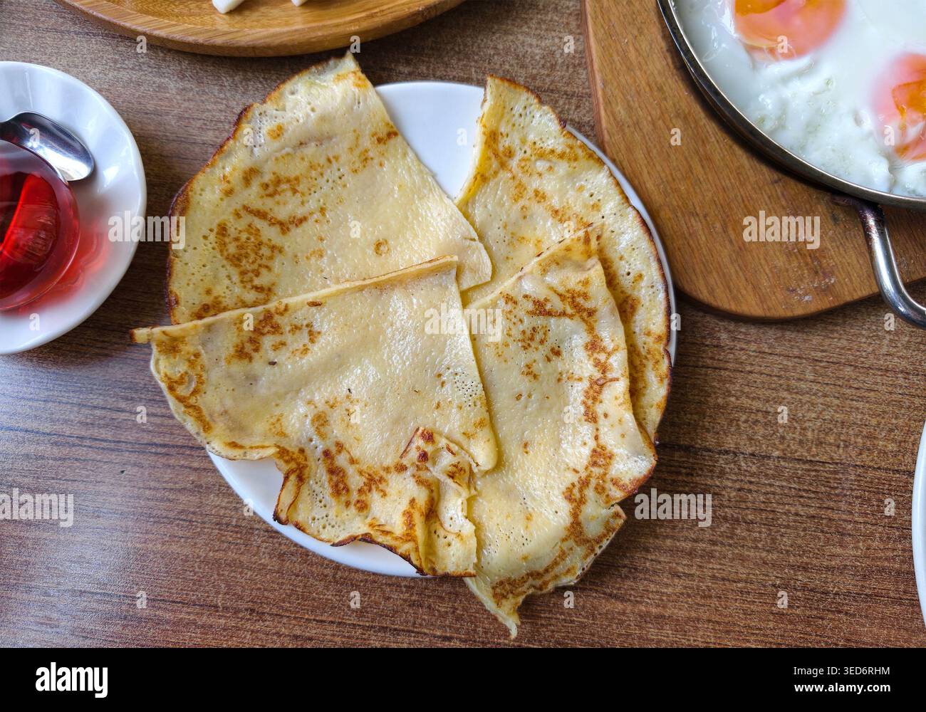 Pfannkuchen sind ordentlich auf einem weißen Teller angeordnet. Sie stehen auf einem Holztisch mit Beilagen in der Nähe. Die Szene zeigt eine Frühstückssituation in einem Lokal Stockfoto