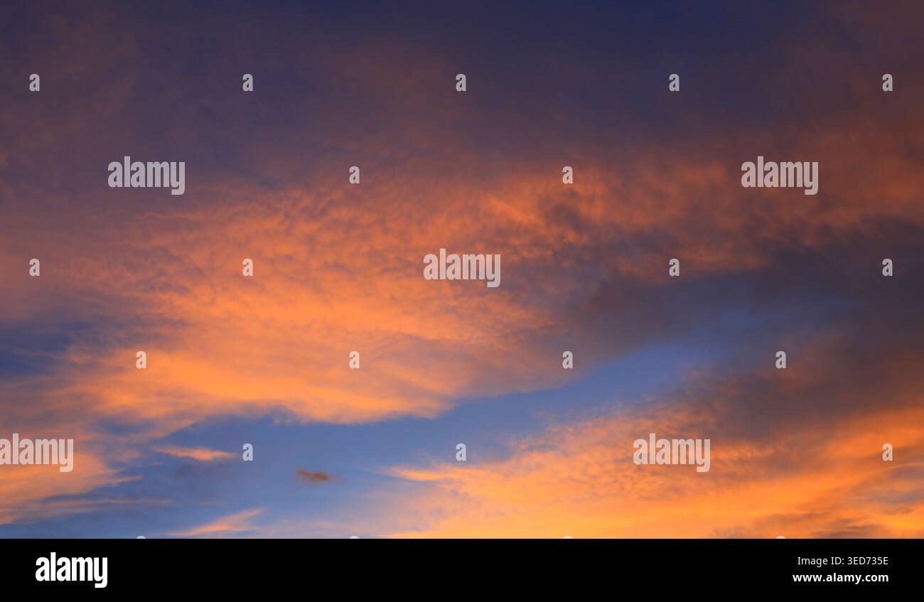 Der Himmel ist voller Wolken, die von den warmen Orange- und Rosa-Tönen beleuchtet werden und sich bei Sonnenuntergang mit tiefen Blautönen kontrastieren Stockfoto