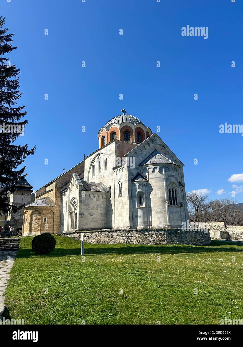 Vorderansicht der Klosterkirche Studenica mit Steinweg und grünem Rasen unter einem klaren blauen Himmel in Serbien. - Smartphone-aufgenommenes Stockfoto
