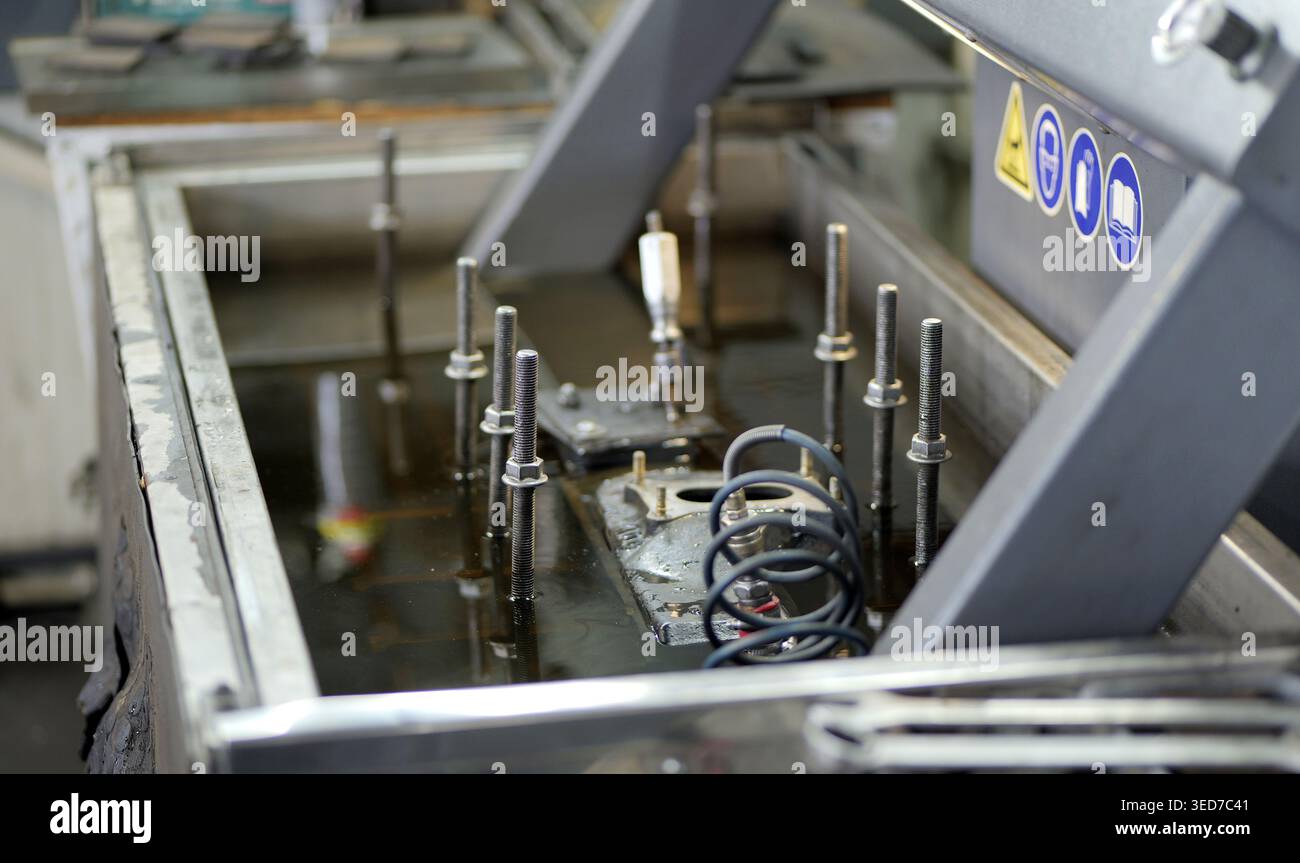 Bei der Leckprüfung des Zylinderkopfs im Wassertank wird ein unter Druck stehendes Bauteil mit Metallrahmen festgestellt, während der Techniker auf Luftblasen überprüft, die auf Risse hinweisen. Stockfoto