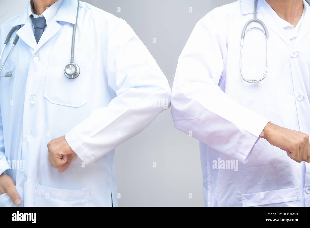 Nahaufnahme zweier Ärzte in Labormänteln und Stethoskopen, die sich gegenseitig mit Ellbogen begrüßen Stockfoto