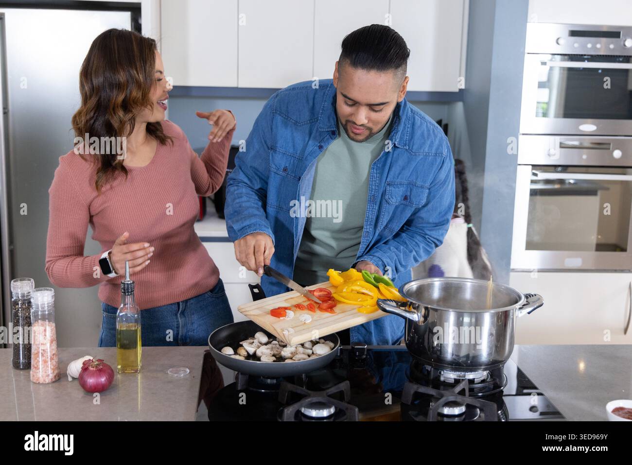 Ein paar Kochen in der modernen Küche, ein Mann, der geschnittene Paprika vom Schneidebrett in die Pfanne schiebt Stockfoto