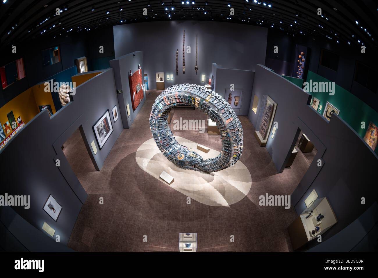 Regenbogenschlangen-Jerry-Can-Skulptur Washington DC Vereinigte Staaten | WASHINGTON — Romuald Hazoumes „Regenbogenschlange (Dan-Ayido-Houedo)“, ein gewundener Ring aus wiederverwerteten Benzinkanistern, dominiert eine Galerie im Nationalmuseum für Afrikanische Kunst in Washington, D.C. Der beninische Künstler vollendete die Skulptur 2007 und stellte eine Schlange dar, die ihren eigenen Schwanz verschlingt, ein Symbol der Fruchtbarkeit und des ewigen Lebenszyklus der Fon und Yoruba, während er auch auf die Ölförderung und den transatlantischen Sklavenhandel in Westafrika anspielt. Stockfoto
