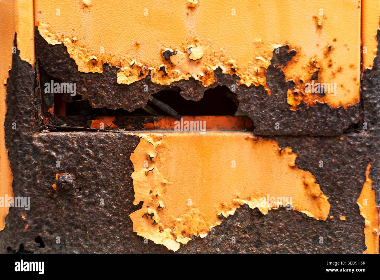 Eine Nahaufnahme zeigt eine verwitterte Metalloberfläche mit abblätternder orangefarbener Farbe und dunklen Rostflecken, die Erosion und Zerfall durch Oxidation und t offenbart Stockfoto