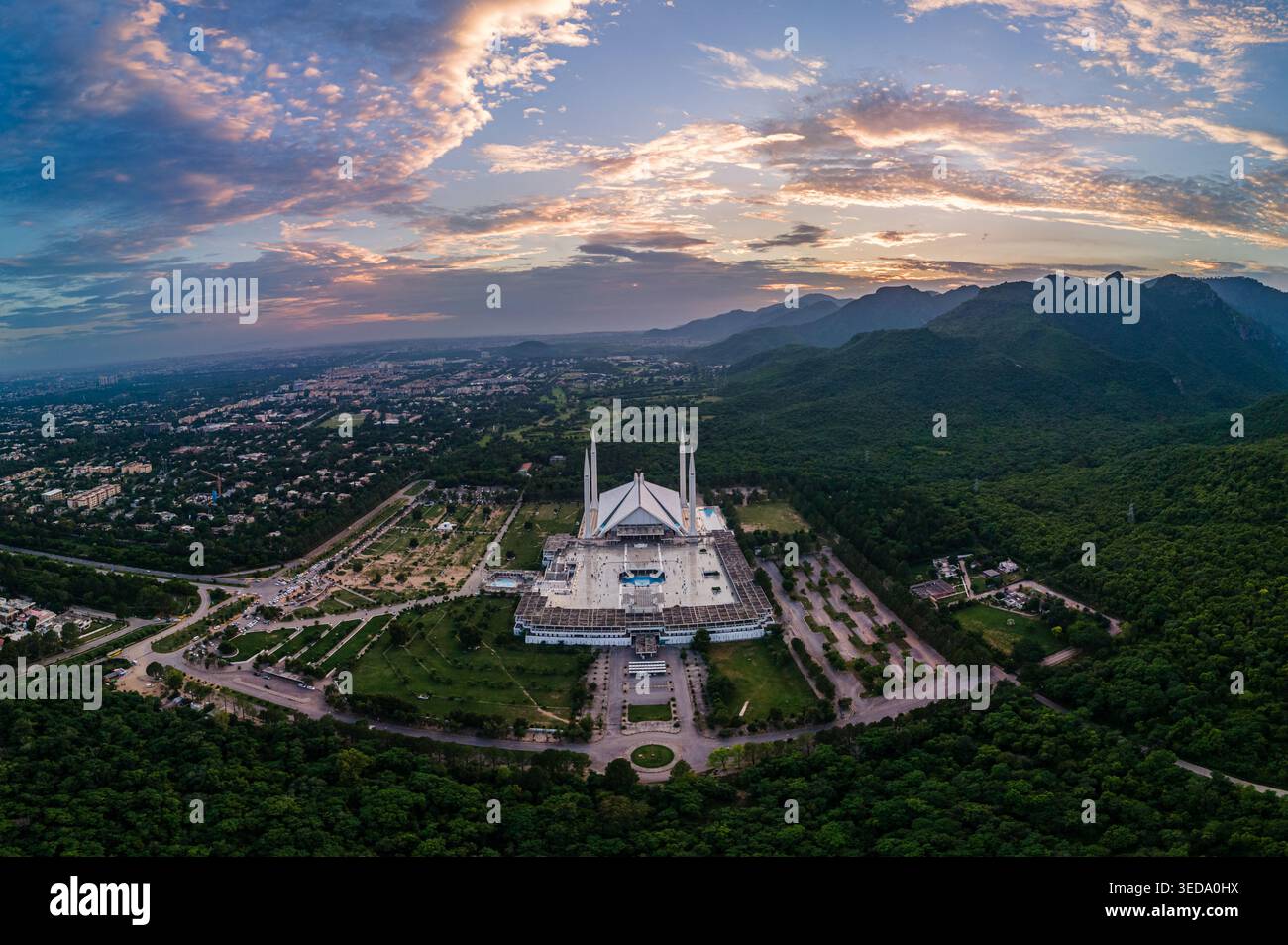 Blick aus der Vogelperspektive auf Faisal Masjid am Fuße der Margalla Hills mit seiner berühmten weißen Marmorarchitektur unter einem lebendigen Sonnenuntergang-Himmel Islamabad, Stockfoto