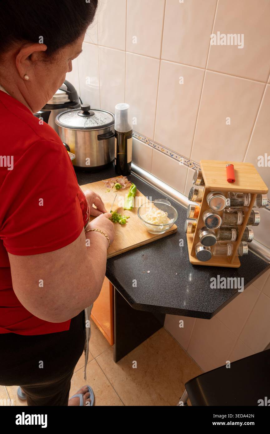 Frau, die grünen Paprika und andere Zutaten auf einem Schneidebrett hackt, eine Mahlzeit zubereitet Stockfoto