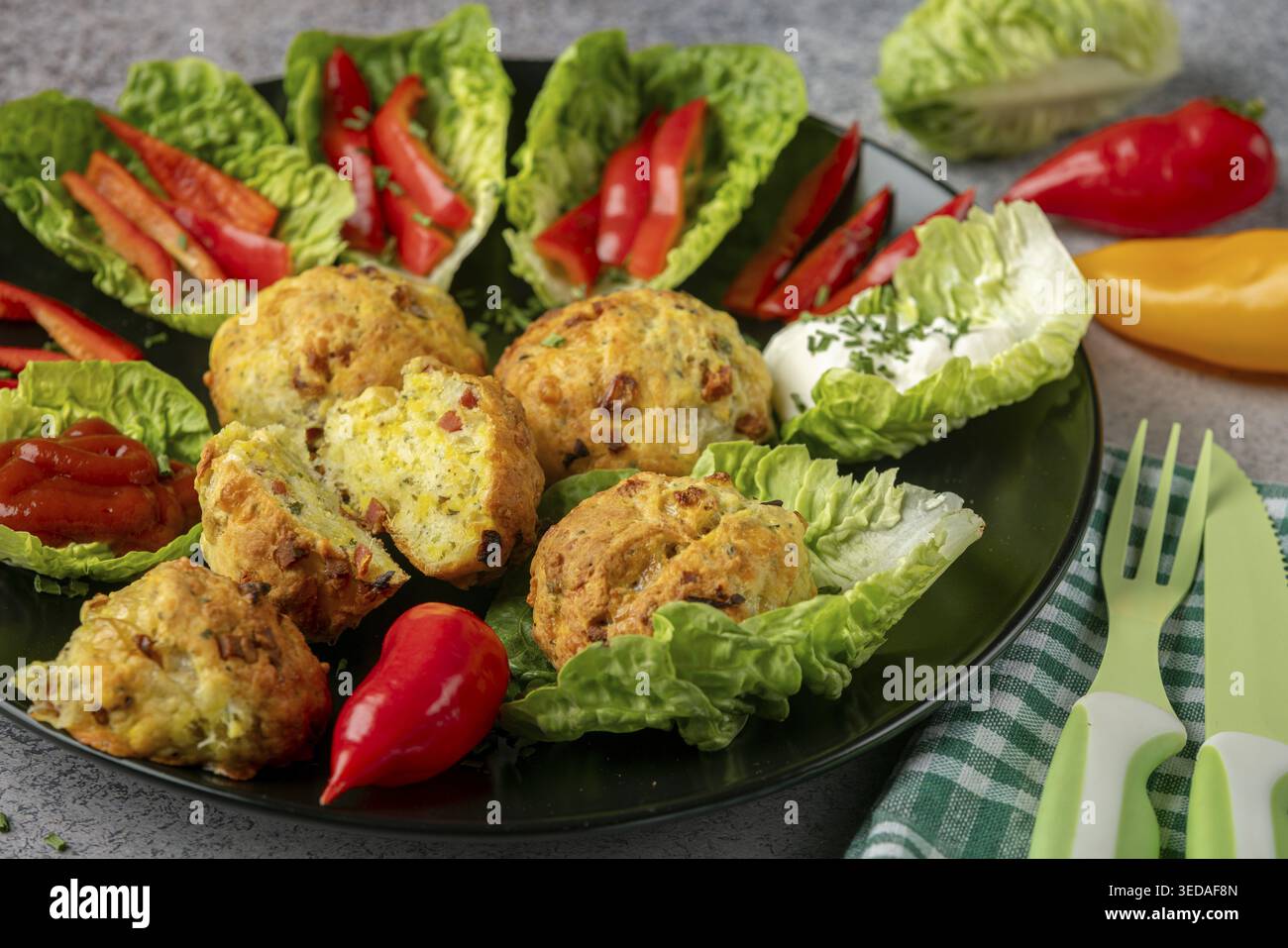 Ein Teller mit gebackenen Bällchen, Pizzabällchen umgeben von Salatblättern, Pfefferstreifen und Dip Stockfoto