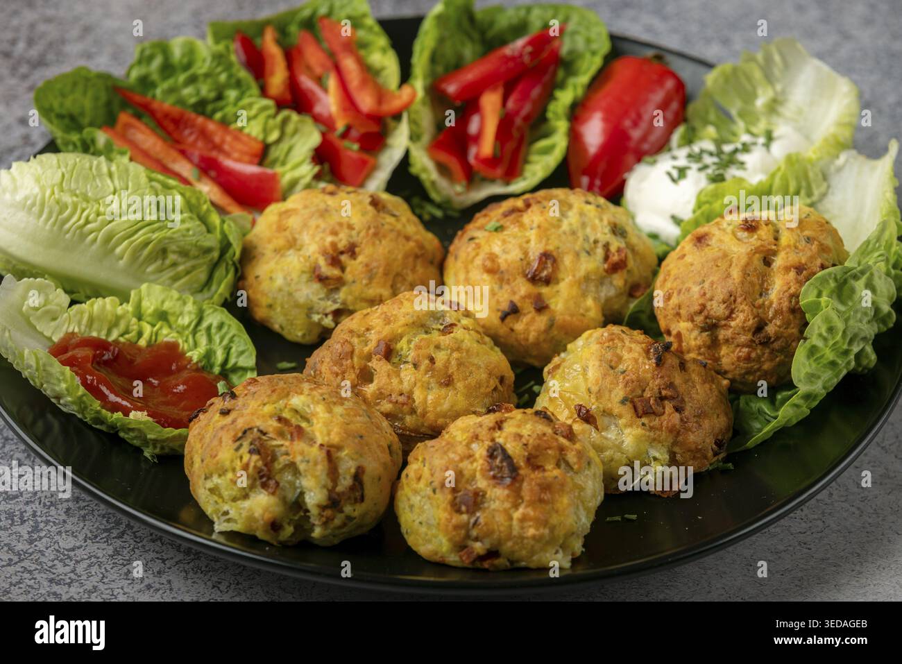 Ein Teller mit gebackenen Bällchen, Pizzabällchen umgeben von Salatblättern, Pfefferstreifen und Dip Stockfoto